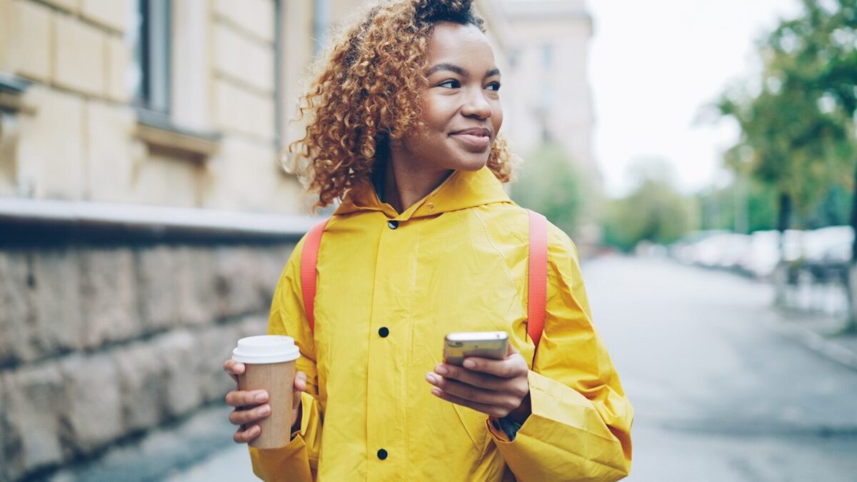 Person walking with coffee in hand talking on mobile phone as part of a daily walking routine habit
